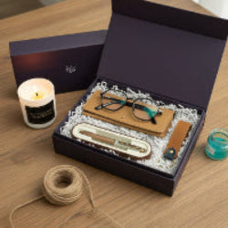 Gift set with eyeglasses, leather strap, and other items in a box on a wooden surface.
