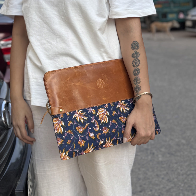 A person holding a brown and multicolored floral patterned leather laptop sleeve.