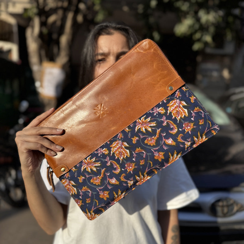 A person holding a laptop case with a geometric pattern in black and white and a tan leather accent.
