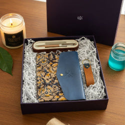 Gift set with blue wallet, patterned fabric, and keychain in a box on a wooden surface.