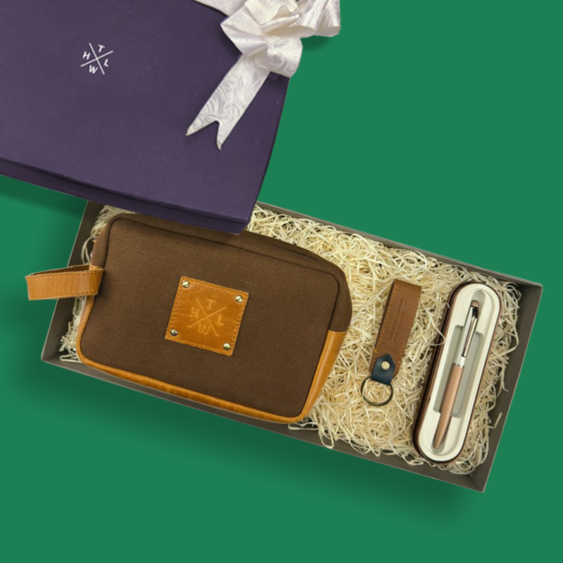 Gift set with brown pouch, pen set, and keychain in a box on a green background