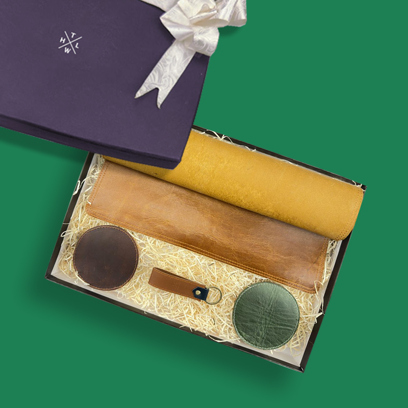 Set of leather items including a desk mat, key chain and coasters in a gift box on a green background.