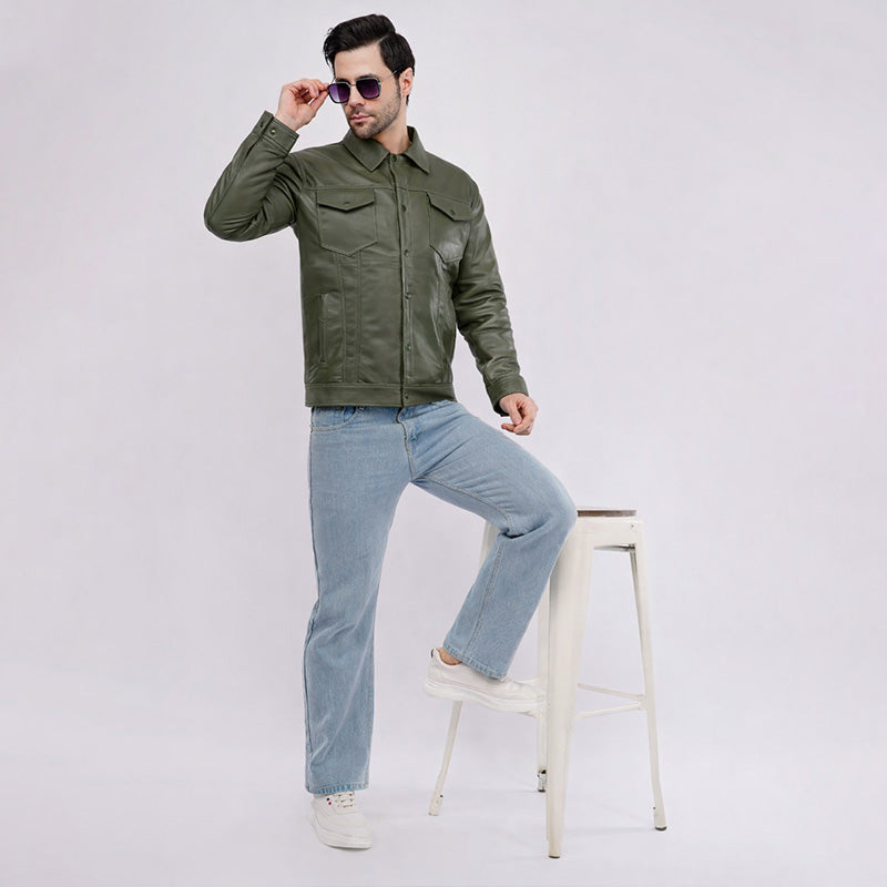 Man wearing a green jacket and light blue jeans, sitting on a white stool against a white background