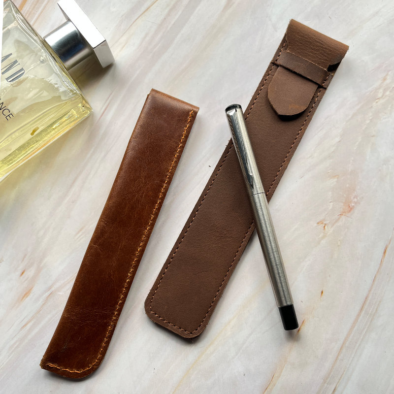 Brown leather pen holder with a silver pen on a light wooden surface