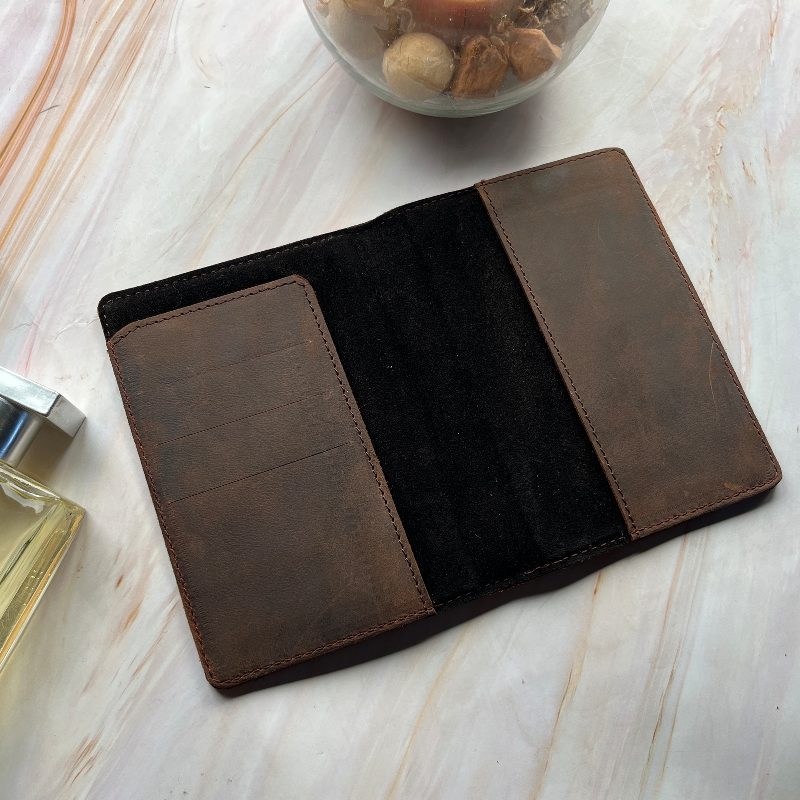 Brown leather wallet on a light wooden surface with a glass container of pebbles in the background.