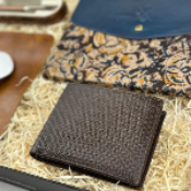 Brown leather wallet on a bed of straw with patterned fabric and phone in the background