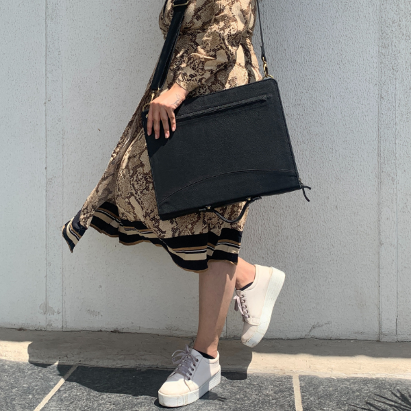 Person holding a black clutch bag against a gray wall
