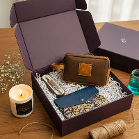 Gift box with a brown wallet, blue pouch, and candle on a wooden surface.