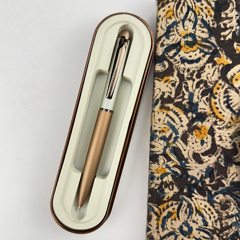 Bronze pen in a case next to a patterned fabric on a white background