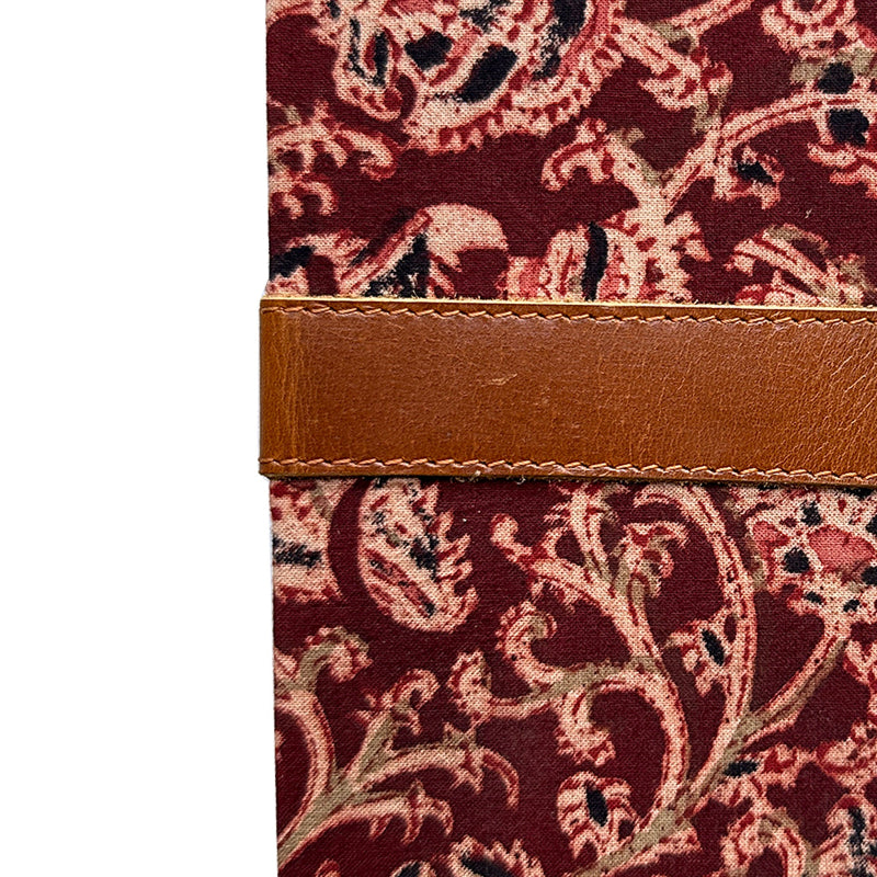 Close-up of a fabric with intricate paisley pattern and brown leather strip on a white background