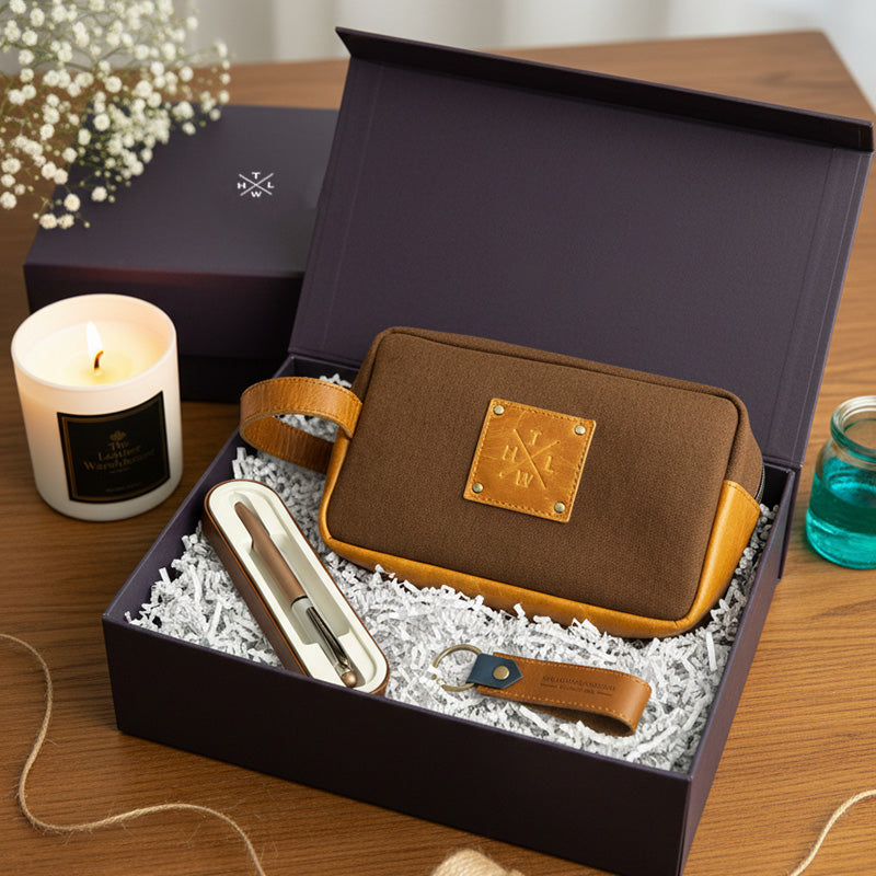 Brown leather pouch with gold accents in a gift box with a candle and glass on a wooden surface.
