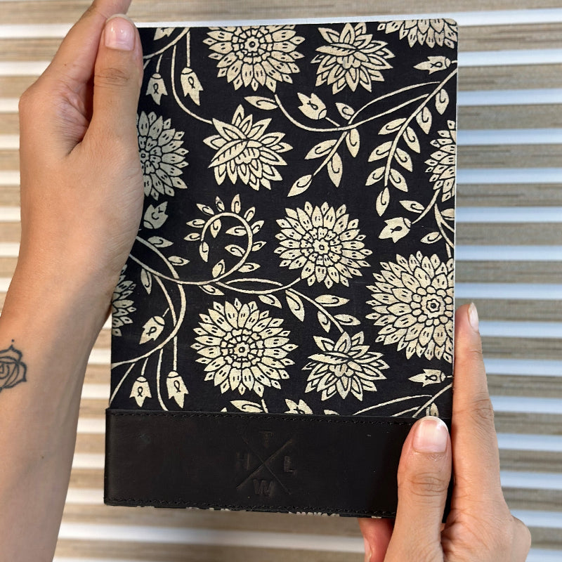 Hand holding a black notebook with white floral pattern