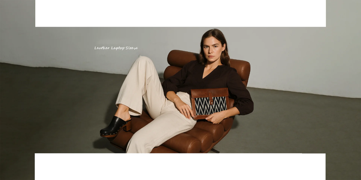 Woman sitting on a brown leather chair holding a patterned pillow against a plain background