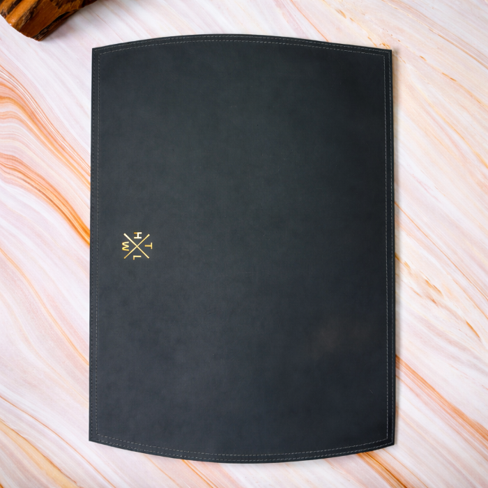 Black PLACEMAT with a gold logo on a marble surface