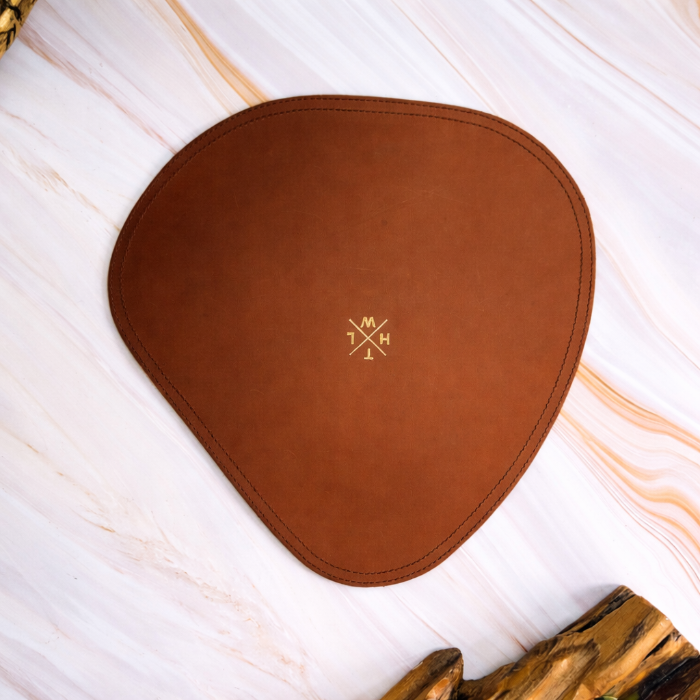 Brown placemat leather heart-shaped pad with a logo on a light wooden surface