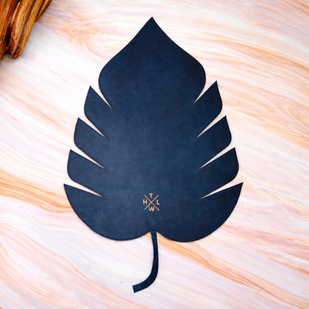 Navy blue leaf-shaped placemat with a logo on a light background