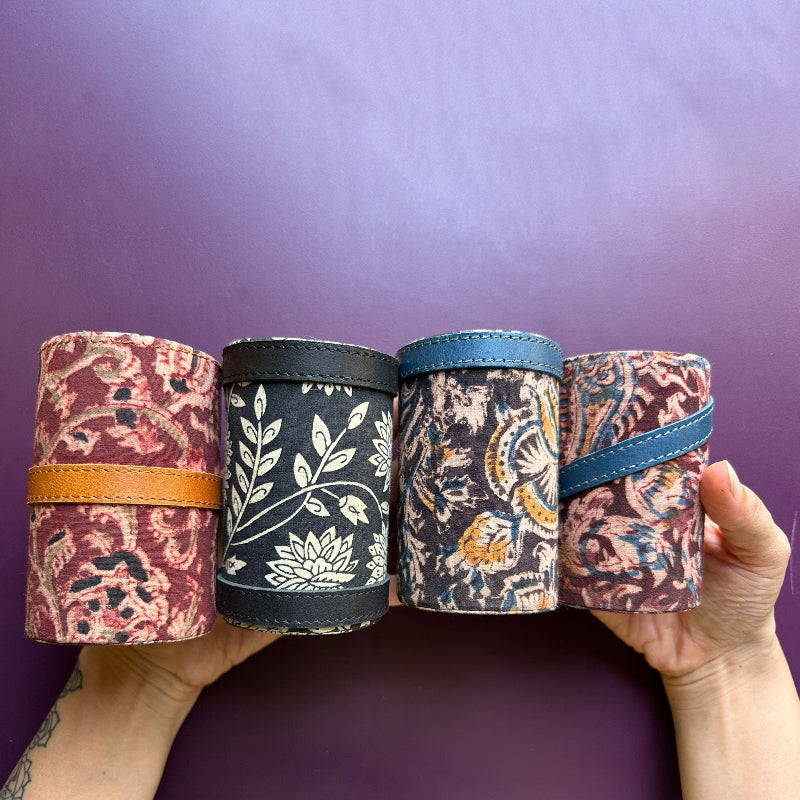 Four fabric-wrapped cylindrical items held against a purple background