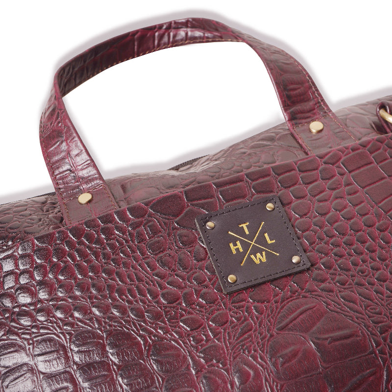 Close-up of a maroon textured handbag with a brand label on a white background
