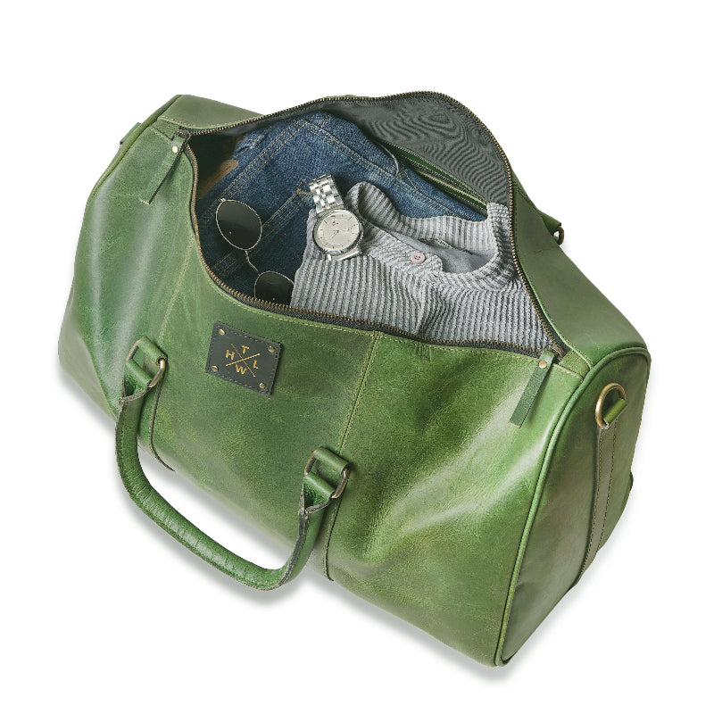 Green leather duffel bag with clothes and accessories on a white background