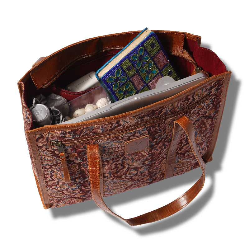 Open brown leather handbag with patterned interior, containing a book and other items on a white background.