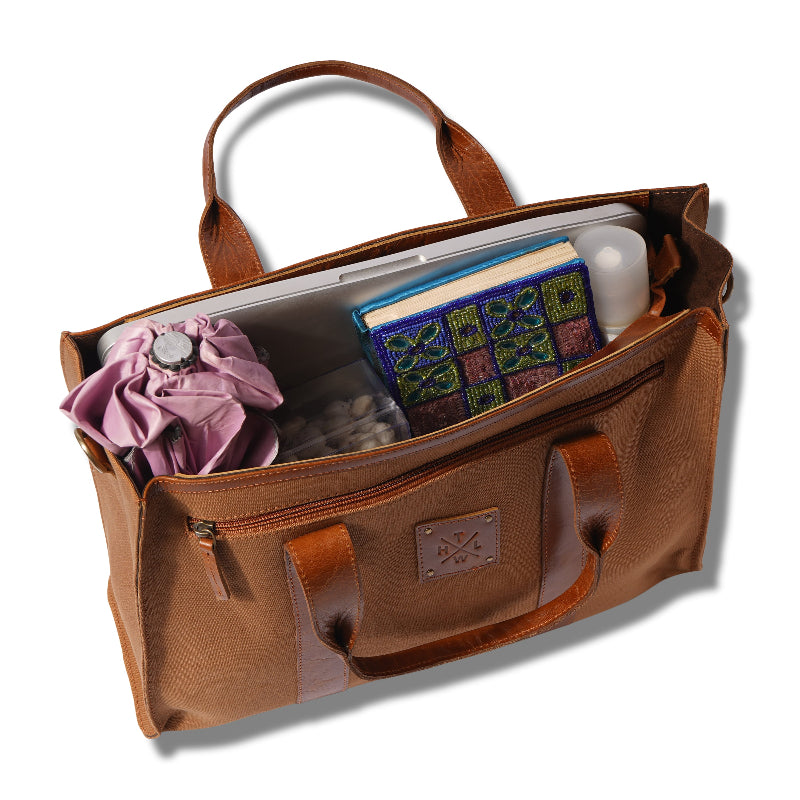 Brown leather bag with items including a book and a pink flower on a white background