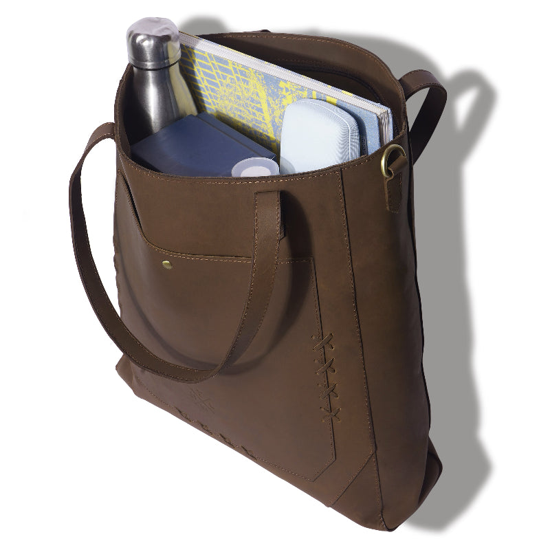 Brown leather tote bag with items including a water bottle and books on a white background
