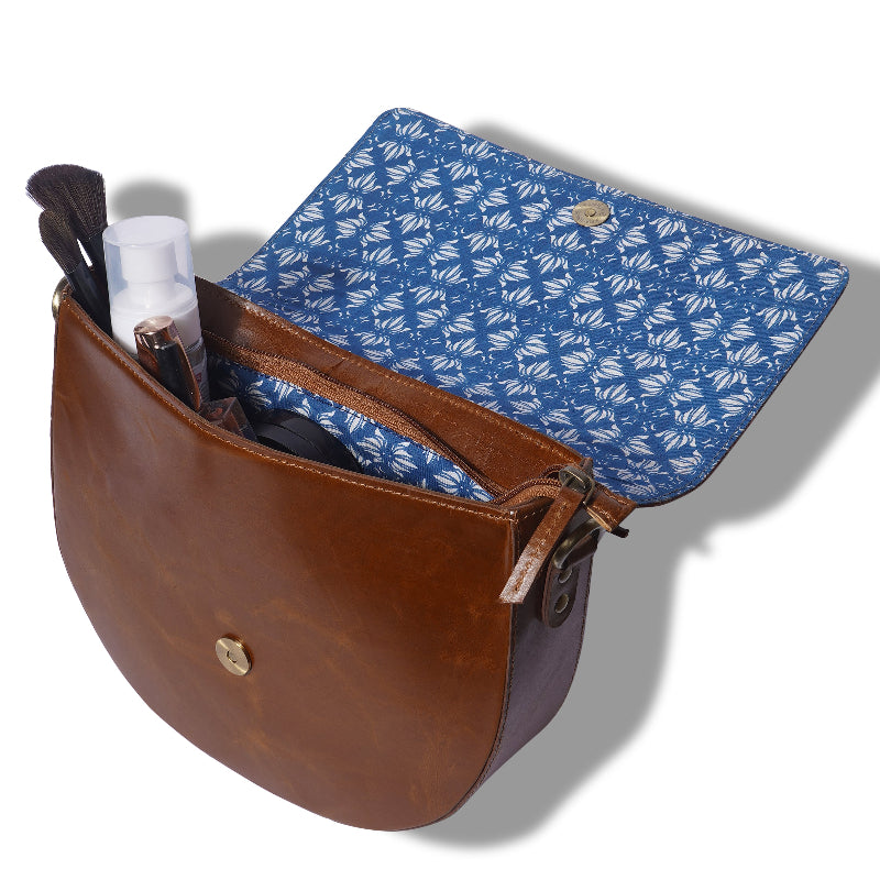 Brown leather bag with blue patterned interior, containing makeup items on a white background