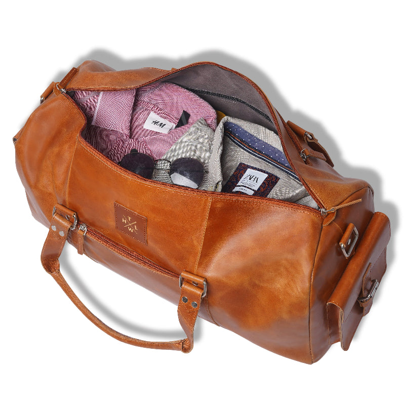 Brown leather duffel bag with clothes spilling out on a white background