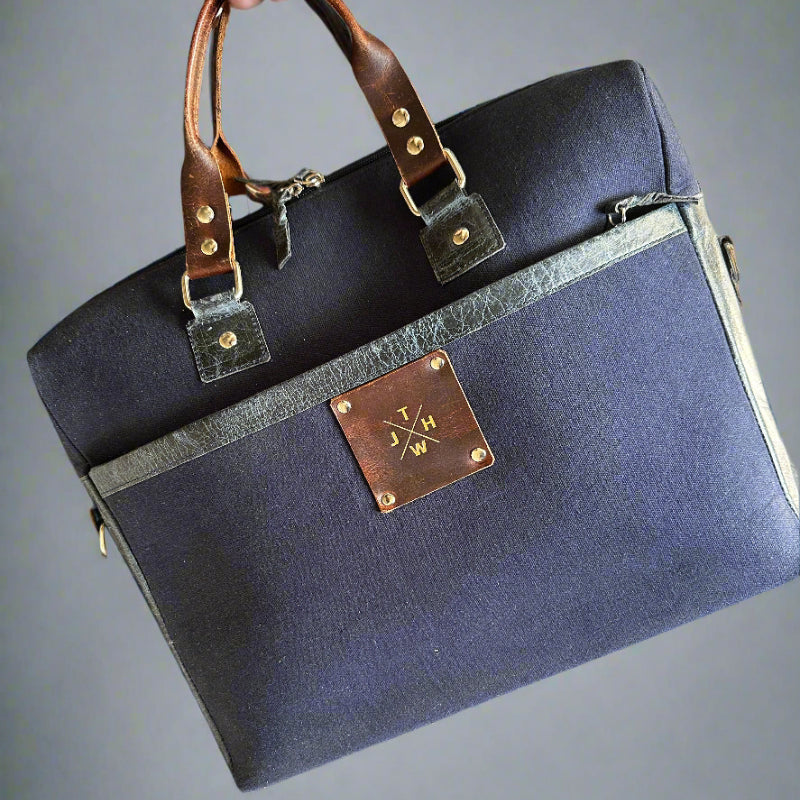 Navy blue bag with brown leather strap and decorative plaque on a textured surface.