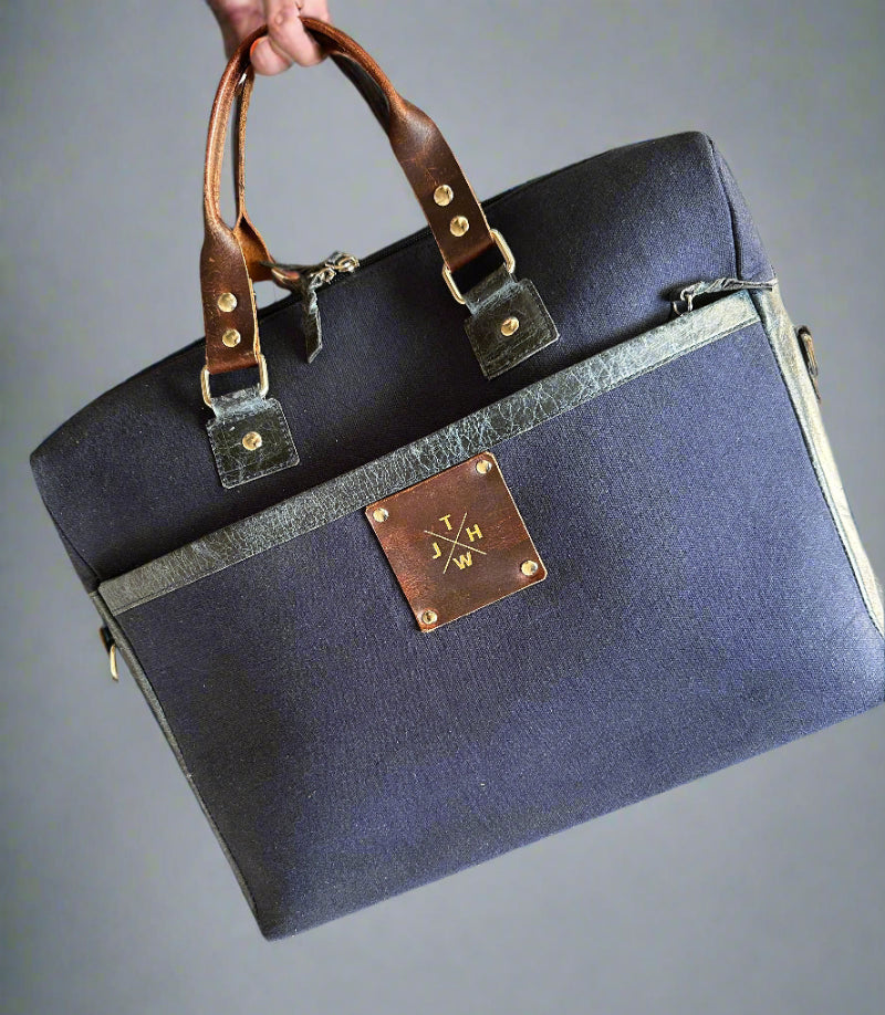 Navy blue bag with brown leather strap and decorative plaque on a textured surface.