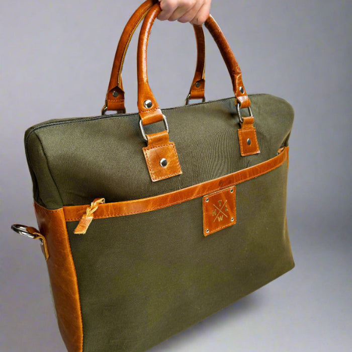 Green bag with brown handles and trim held by a hand against a gray background