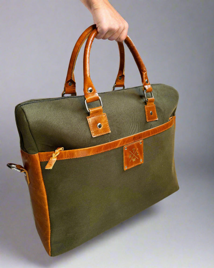 Green bag with brown handles and trim held by a hand against a gray background