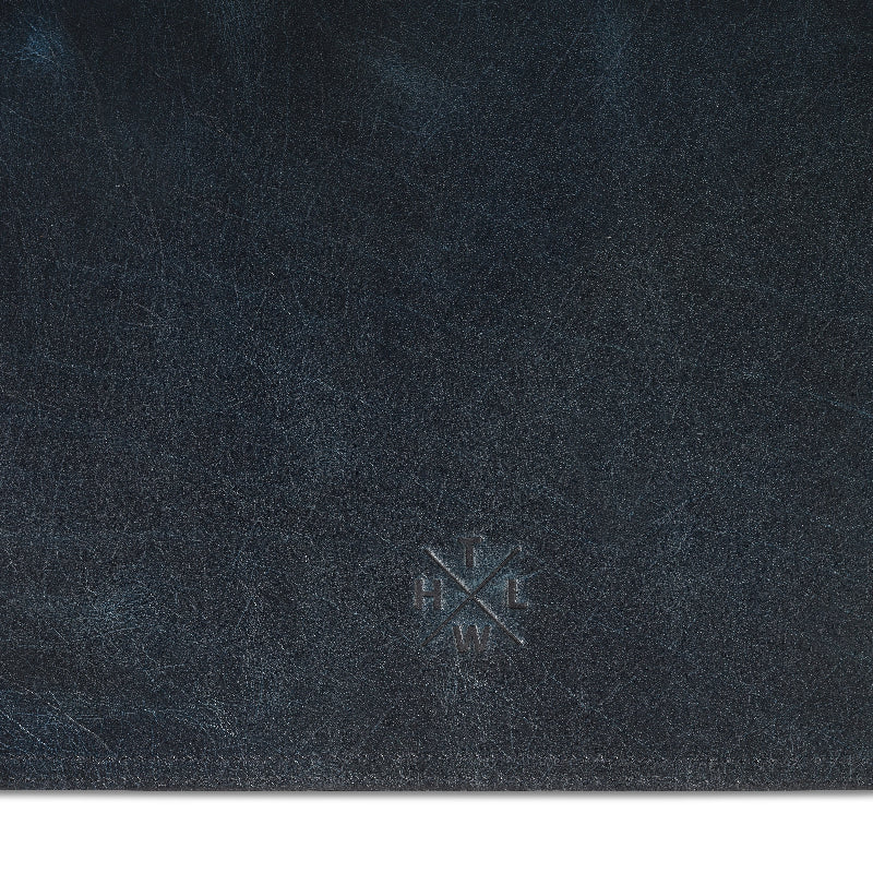 Close-up of dark blue leather desk mat with a logo in the center.
