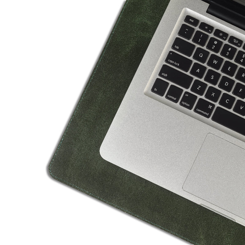 Laptop on a green leather desk pad with a white background