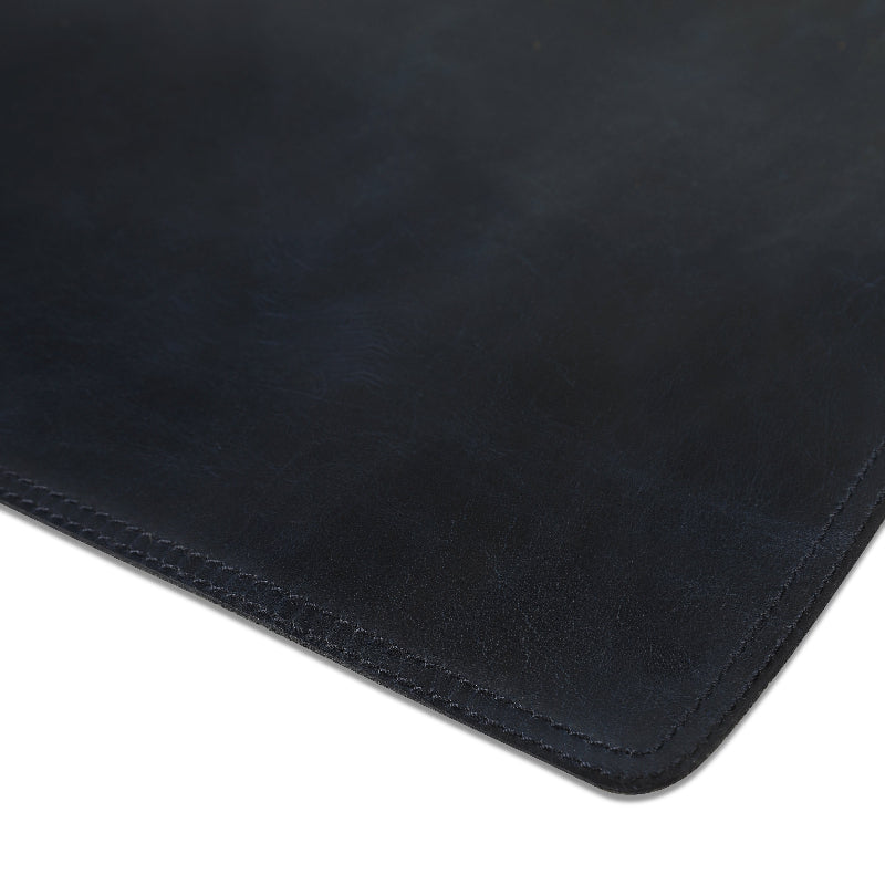 Close-up of a black leather desk mat with visible texture and stitching.