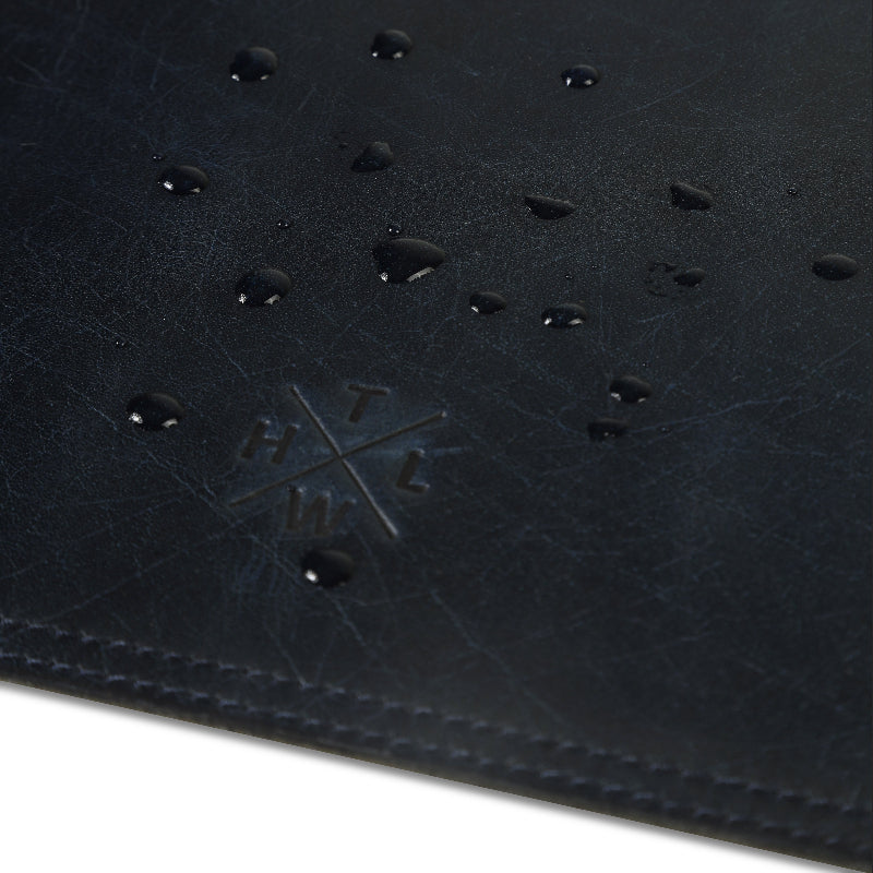 Close-up of a black leather desk mat with a brand logo, on a white background
