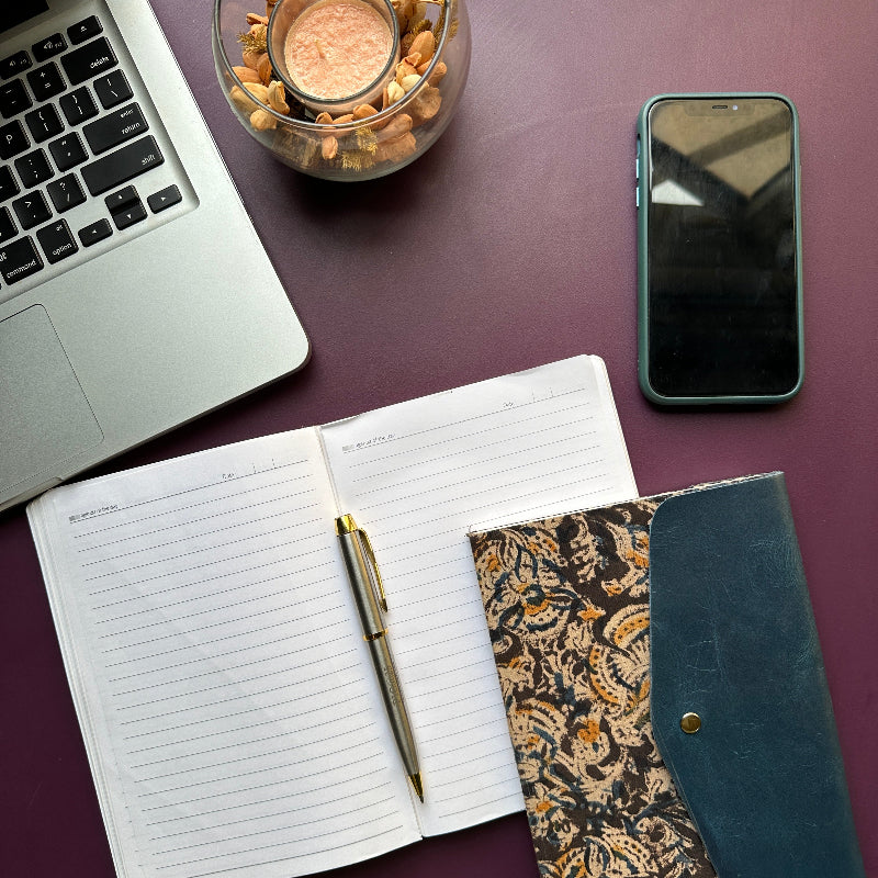 Laptop, notebook, pen, phone, and decorative items on a purple surface