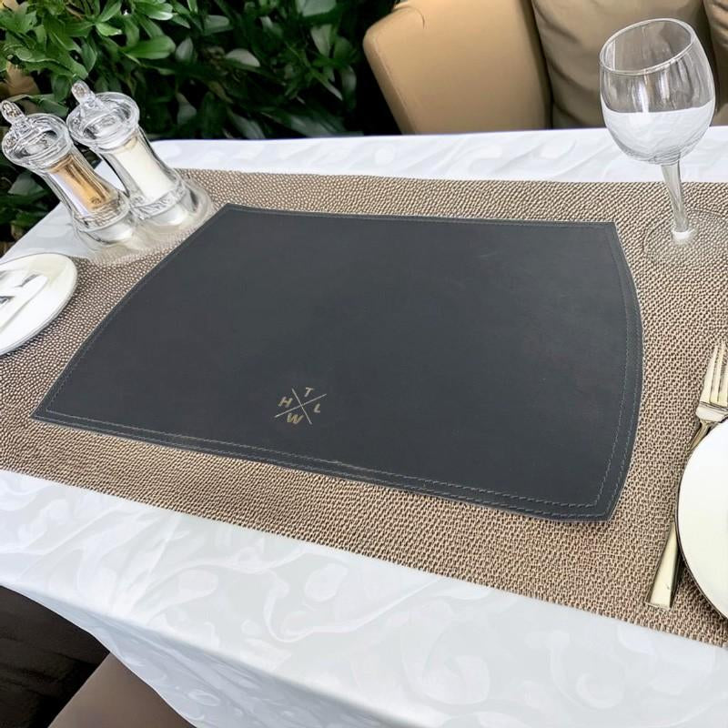 A gray leather placemat on a set dining table with a glass of wine and cutlery on top.
