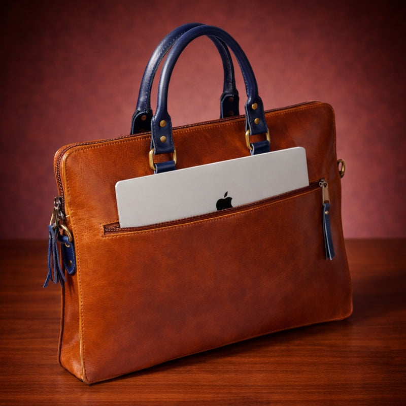 Brown leather handbag with blue handles holding an Apple laptop on a wooden surface.