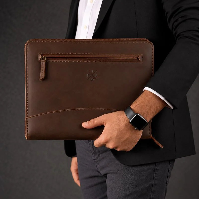 Man in a blazer holding a closed brown leather zip portfolio.