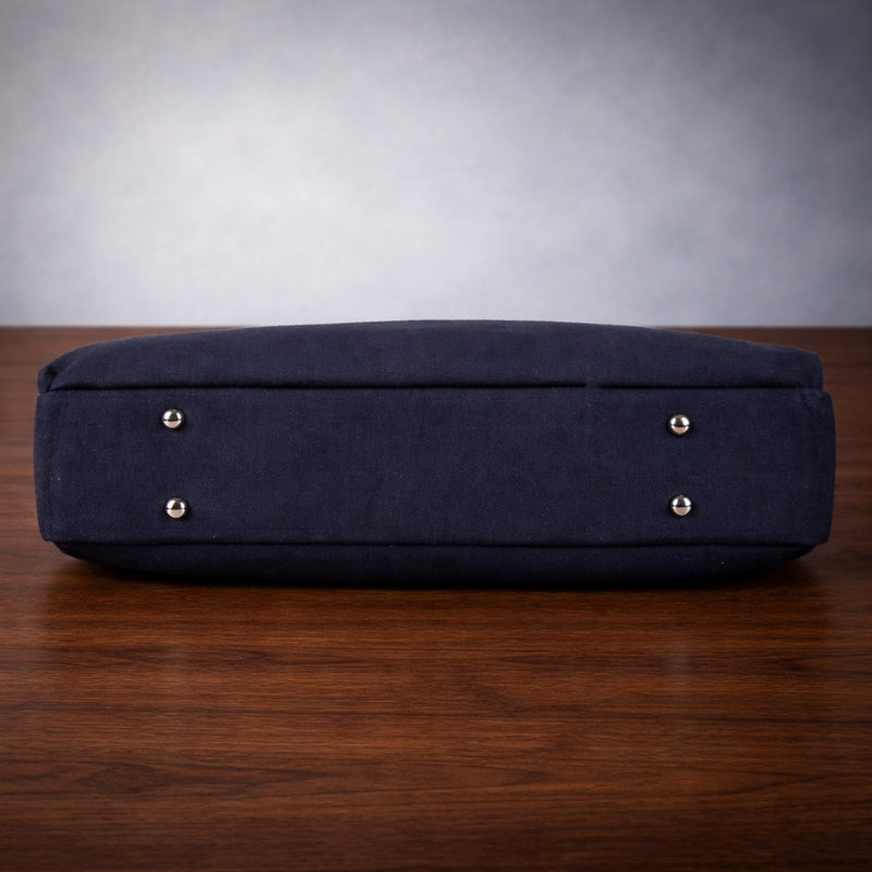 Navy blue canvas bag with gold studs on a wooden surface and gray background