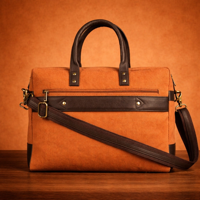 Orange canvas & leather briefcase with black accents on a wooden surface and orange background