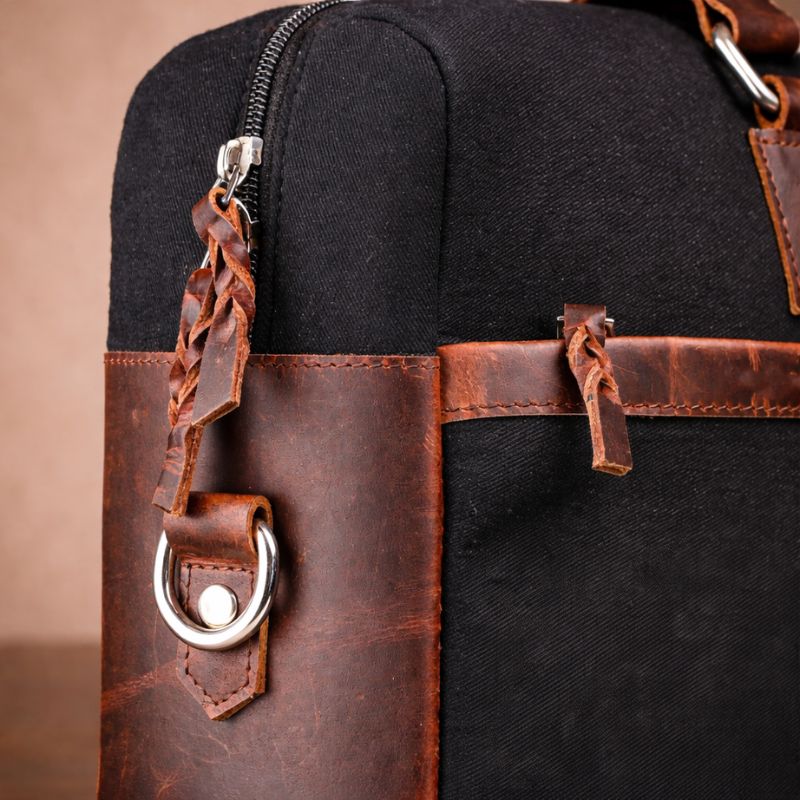 Black canvas bag with brown leather straps and accents on a beige background