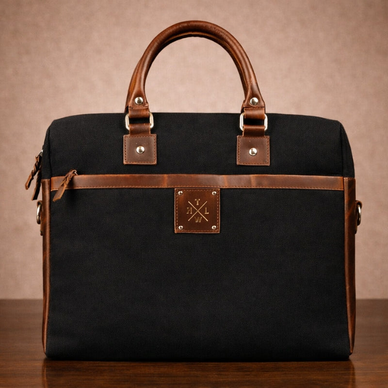 Black canvas bag with brown leather accents on a wooden surface and beige background