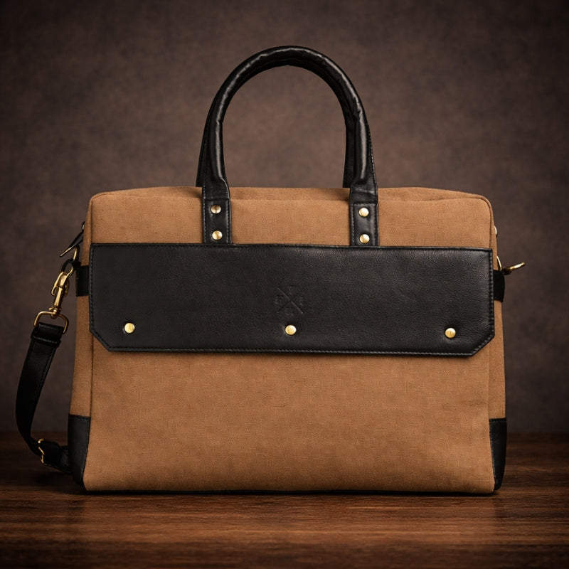 Brown canvas and black leather bag with gold studs on a wooden surface and dark background