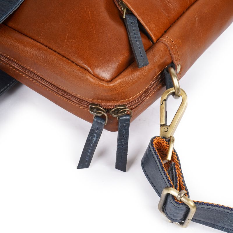 Close-up of a Tan leather bag with a gold clasp and blue strap on a white background