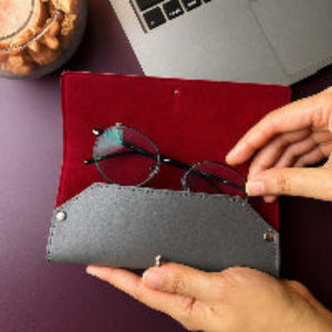 Person holding a gray eyeglass case with glasses on a red surface, next to a laptop and snacks.