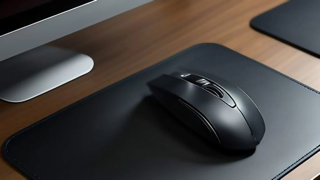 Black computer mouse on a black mouse pad with a monitor in the background