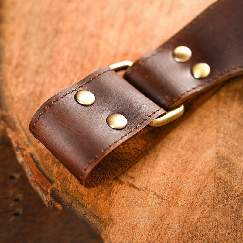 Close-up of a brown leather strap with gold rivets on a wooden surface