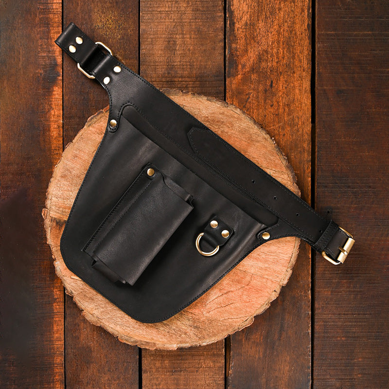 Black leather belt bag with gold hardware on a wooden surface